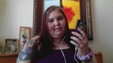 sarcoidosis and therapy | Sarcoidosis News | Photo shows Kerry looking at a phone in her hand, with headphone wire visible from her ears to the phone.