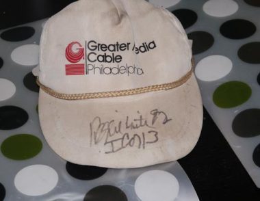 A white hat features the logo for Greater Media Cable Philadelphia, and on the brim is NFL player Reggie White's signature.